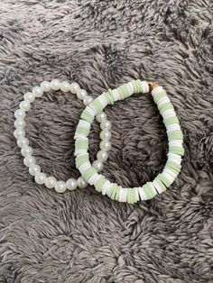 two bracelets with pearls and green beads on a gray carpeted surface in close up