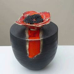 a black vase with a red flower on it