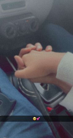 someone is holding the hand of another person in a car while they are using their cell phone