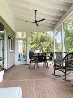 a porch with chairs, table and ceiling fan on the back side of the house