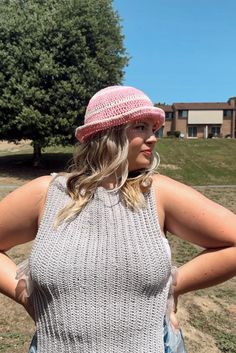 a woman wearing a pink hat standing in front of a tree with her hands on her hips