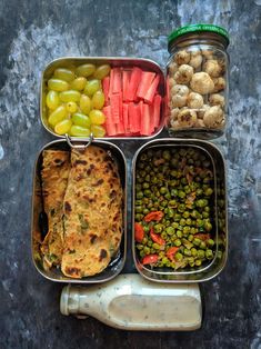 an assortment of food is arranged in four separate trays, including vegetables and bread