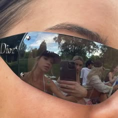 a woman wearing mirrored sunglasses with her reflection in the lens and people standing behind her