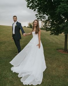 a bride and groom holding hands in the grass