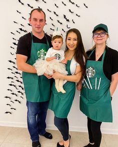 three people wearing green aprons and holding a baby in front of a wall with bats on it