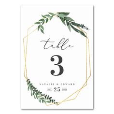 a table number card with greenery and gold foil on the front, in an octagonal frame