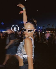 a woman in white sunglasses standing on top of a field next to a crowd at night