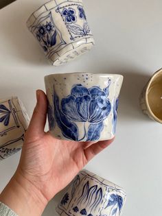 a hand holding a blue and white cup with flowers on it next to other cups