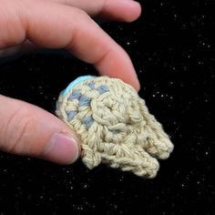 a hand holding a small crocheted object in it's left hand, against a black background