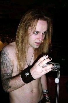 a shirtless man with long hair holding a cell phone in his right hand and looking at the camera