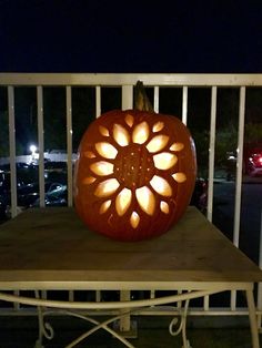 a pumpkin carved to look like a flower on top of a wooden table in front of a balcony