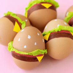 six eggs decorated like hamburgers on a pink surface