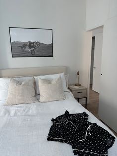 an unmade bed with white sheets and black polka dot pants on it, in a bedroom