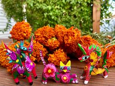 three colorfully decorated figurines sitting on top of a wooden table next to orange flowers