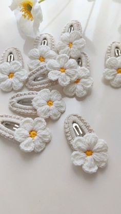 white crocheted flower clips with yellow centers on a white surface next to flowers