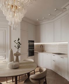 an elegant kitchen with white cabinets and chandelier hanging from the ceiling, along with a round dining table surrounded by beige chairs