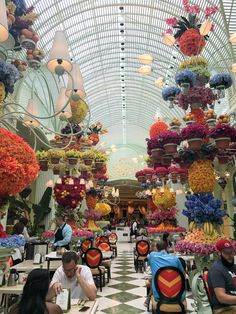 people are sitting at tables in the middle of a flower covered building with lots of flowers hanging from the ceiling