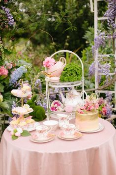 a table topped with lots of cakes and cupcakes on top of a pink table cloth