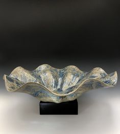 a white and blue bowl sitting on top of a wooden stand in front of a black background