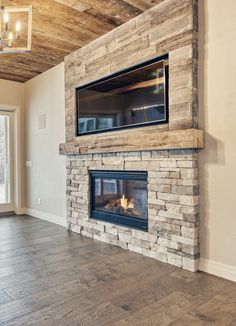 an empty living room with a fireplace and tv mounted on the stone wall above it