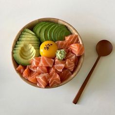 a wooden bowl filled with assorted fruits and veggies next to a spoon