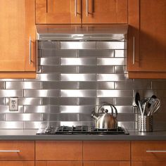 a kitchen with wooden cabinets and stainless steel tile backsplash, tea kettle on the stove