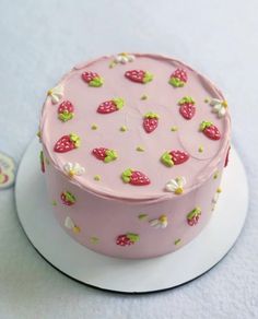 a pink cake with strawberries and flowers on it sitting on a white platter