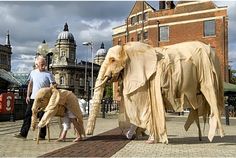 two people are standing next to sculptures of elephants on the sidewalk in front of a building