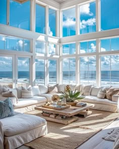 a living room filled with lots of white furniture and large windows overlooking the ocean on a sunny day