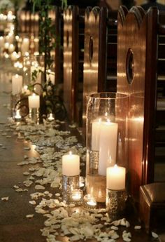 candles are lined up on the floor in front of pews with petals scattered around them