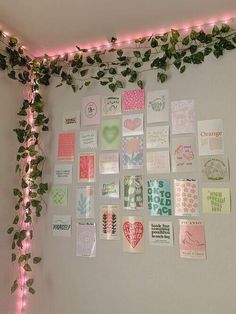 a wall covered in lots of different types of cards and plants next to a pink light