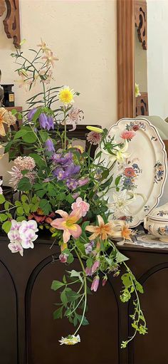 a vase filled with lots of flowers sitting on top of a wooden dresser next to a mirror