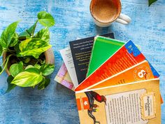 there are many books on the table next to a cup of coffee and a potted plant