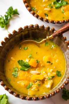 two bowls filled with yellow soup and garnished with cilantro, parsley