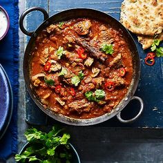 a pan filled with meat and vegetables next to some pita bread on a table