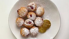 a white plate topped with powdered sugar covered pastries and a gold coin next to it