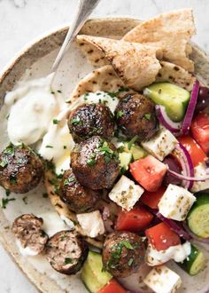 a bowl filled with meatballs, vegetables and pita bread on top of a table