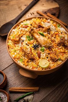 a bowl filled with chicken and rice on top of a wooden table next to spoons