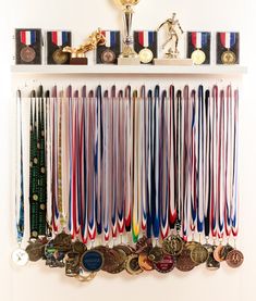 a white shelf filled with lots of medals on top of a wooden floor next to a trophy