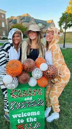 three women dressed in animal costumes holding a welcome to the zoo sign with balloons on it