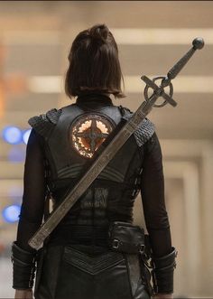 a woman holding two swords in her hands and looking down at the ground while wearing black leather