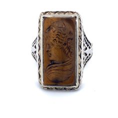 All of our jewelry is guaranteed authentic by our Graduate Gemologist of the Gemological Institute of America (GIA). 14k White Gold Filigree Genuine Natural Tiger's Eye Cameo Ring (#J4989) Art Deco 14k white gold filigree ring featuring a carved tiger's eye quartz cameo. The tiger's eye stone measures about 19.1mm x 10mm. The ring fits a size 5 3/4 finger. It weighs 3.2 dwt., and dates from the 1920's. Fantastic! Inv#RZ5350. SKU#J4989. 100% Satisfaction Guaranteed! Antique Carved Sterling Silver Signet Ring, Antique Brown Carved Jewelry, Antique Sterling Silver Intaglio Jewelry, Antique Filigree Ring With Cabochon For Gift, Antique Filigree Cabochon Ring As Gift, Sterling Silver Intaglio Engraved Ring For Formal Occasions, Formal Sterling Silver Engraved Ring With Intaglio, Antique Filigree Cabochon Ring Gift, Antique Engraved Sterling Silver Ring