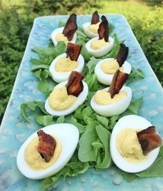 deviled eggs with bacon and spinach are arranged on a blue platter outdoors