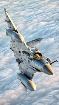 a fighter jet flying through the sky above clouds