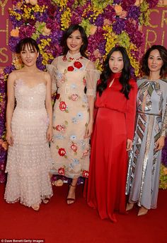 three women standing next to each other in front of a flower covered wall with purple and yellow flowers