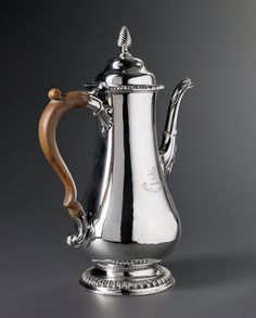 a silver coffee pot with a wooden handle on a metal stand in front of a gray background