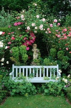 a white bench sitting in the middle of a lush green garden filled with pink and white flowers