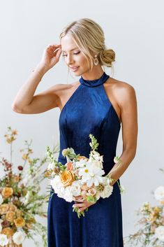 a woman in a blue dress holding a bouquet of white and yellow flowers with her hands behind her head