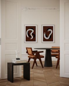 two paintings hang on the wall next to a table and chairs in a room with wood flooring