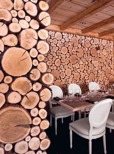 the dining room is set with white chairs and wood slices on the wall behind it